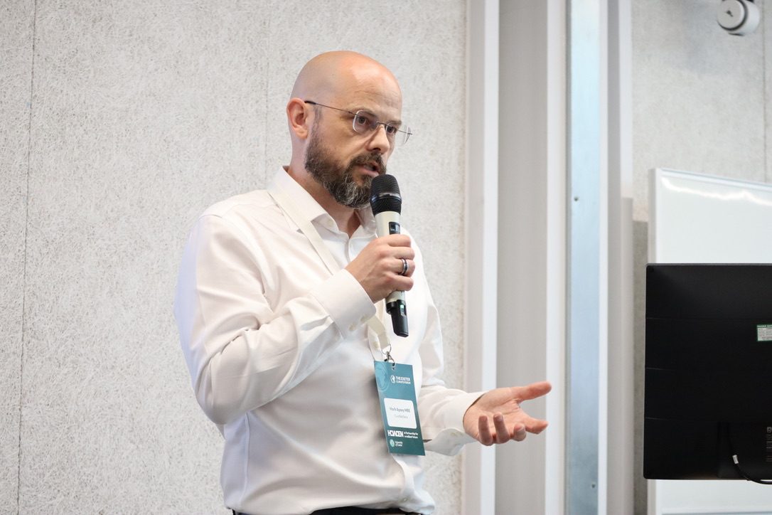 Mark Apsey speaking with a microphone at a conference
