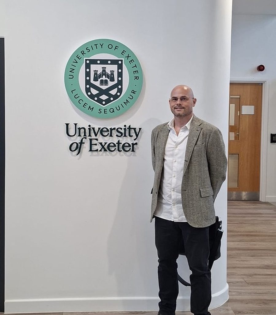 Mark Apsey beside the University of Exeter crest